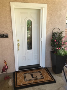 White door, decorative window, "L" mat, potted plant.