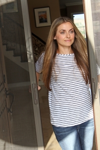 Woman in striped shirt and jeans at open doorway.