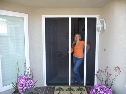 Woman in orange shirt at home doorway with screen door.